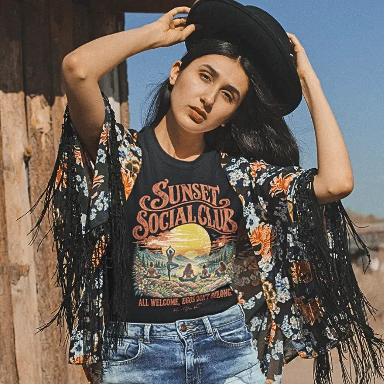 Person wearing the Sunset T-Shirt, Sunset Social Club design, outdoors against a wooden wall, in Black.