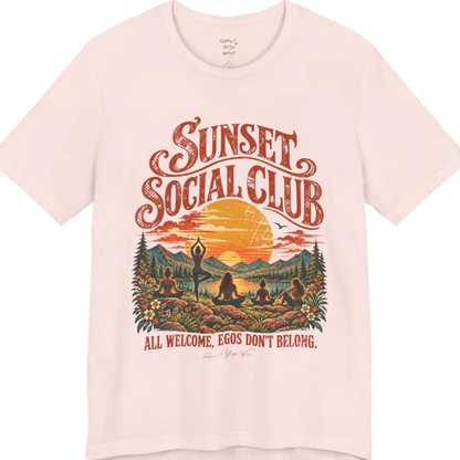A short sleeved tee called the Sunset T-Shirt, flat lay and a Bella + Canvas 3001 shirt. Simply says, Sunset Social Club, All Welcome, Egos Don't Belong. Design highlights several people meditating together across a mountain landscape at sunset, with a large setting sun, pine trees, and florals, in a color vintage travel-poster illustration. Color is Soft Pink. 