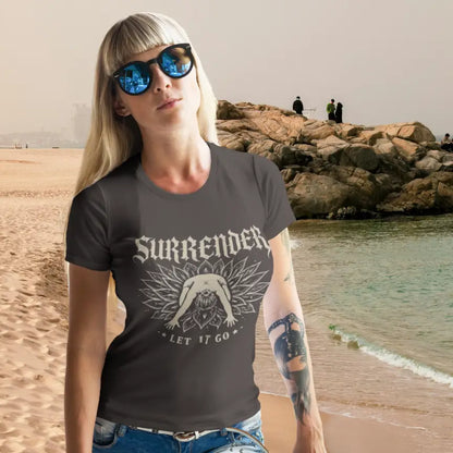 Surrender T-Shirt in Dark Chocolate worn by woman at rocky beach featuring vintage yoga graphic and soulful coastal lifestyle aesthetic.