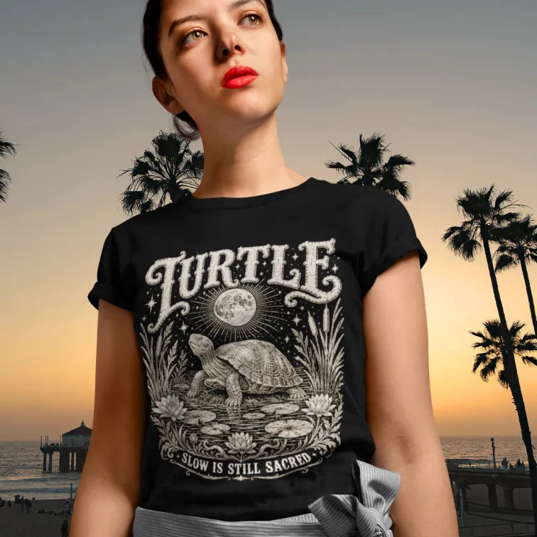 Woman wearing Turtle T-Shirt at the beach at sunset with palm trees behind her, shirt in black.
