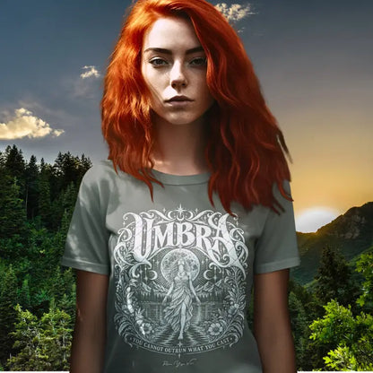 Woman wearing Umbra T-Shirt outdoors at sunset with a mountain forest backdrop, color Heather Military Green.