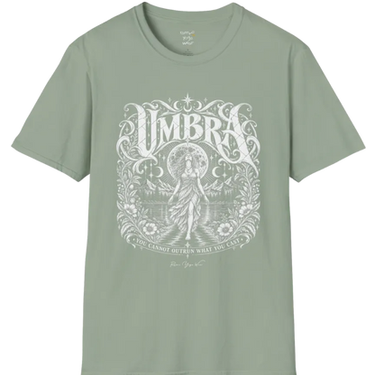 A short sleeved tee called the Umbra T-Shirt, flat lay and a Gildan 64000 shirt. Simply says, You Cannot Outrun What You Cast. Design highlights a moon goddess walking across still water toward distant mountains, framed in ornate vintage lettering with botanical detailing. Color is Sage.