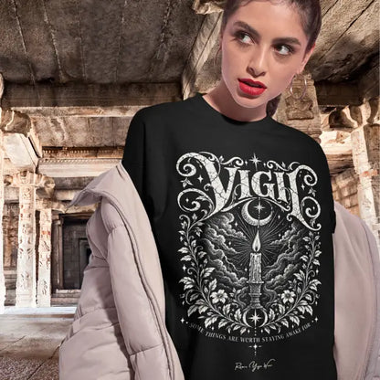 A woman walking through a temple stands under a stone archway, wearing the Vigil T-Shirt. Vigil T-Shirt is a Gildan 64000 and the color is Black.
