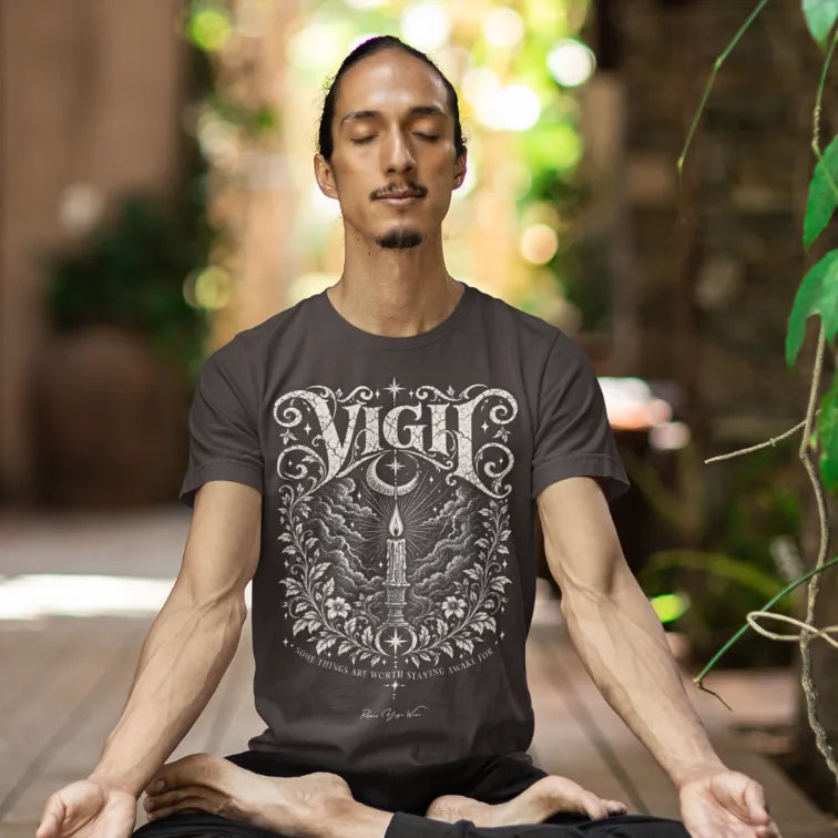 A man sits in meditation with his eyes closed surrounded by greenery, wearing the Vigil T-Shirt. Vigil T-Shirt is a Gildan 64000 and the color is Dark Chocolate.