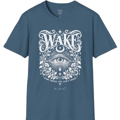 A short sleeved tee with an illustration of a single open eye amid darkness with a dewdrop caught mid-fall beneath it, faint stars scattered around, fine botanical framing at the base. Wake T-Shirt flat lay is a Gildan 64000 and the color is Indigo Blue.
