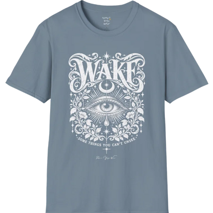 A short sleeved tee with an illustration of a single open eye amid darkness with a dewdrop caught mid-fall beneath it, faint stars scattered around, fine botanical framing at the base. Wake T-Shirt flat lay is a Gildan 64000 and the color is Stone Blue.