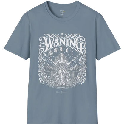 A short sleeved tee called the Waning T-Shirt, flat lay and a Gildan 64000 shirt. Simply says, Waning, Letting Go Isn't The Same As Disappearing. Design highlights a vintage-engraved crest of a robed figure with long flowing hair and open hands releasing petals beneath five moon phases, with mountains, a still lake, stars and ornate floral framing. Color is Stone Blue.