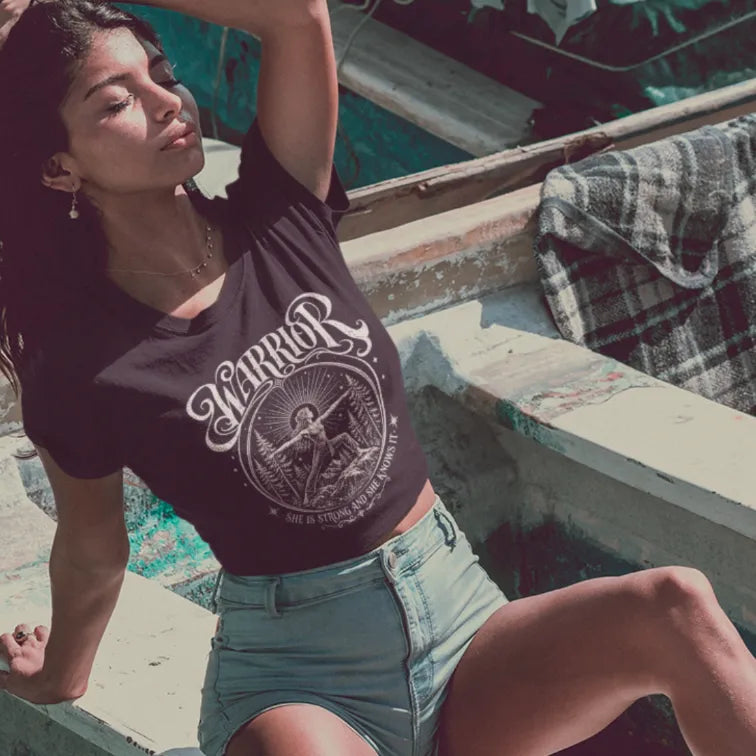 Woman wearing Black Warrior T-Shirt, (tucked under)  in relaxed sunlit boat setting with vintage-inspired mindful lifestyle aesthetic.