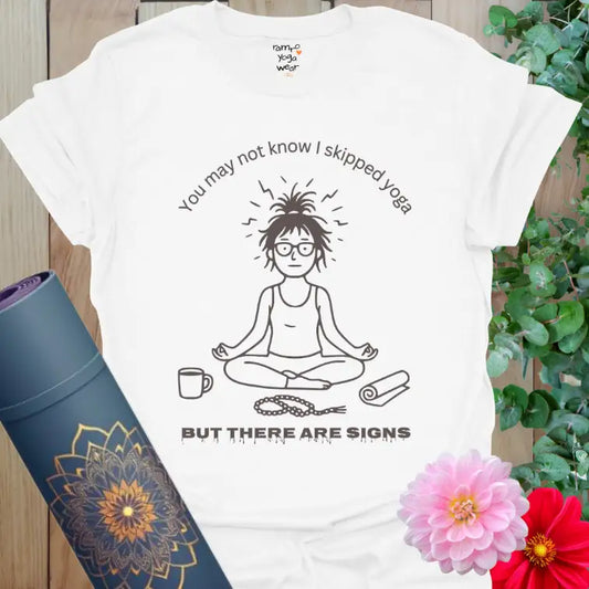 White Signs T-Shirt with line-art yogi sitting cross-legged beside a coffee cup, tangled mala beads, and half-unrolled mat. Funny yoga shirt with mindful humor.